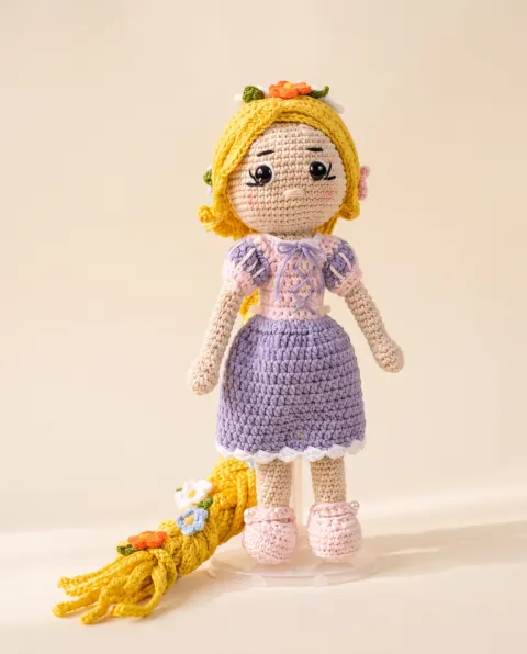 Muñeca de trenza dorada con flores tejidas y vestido lila